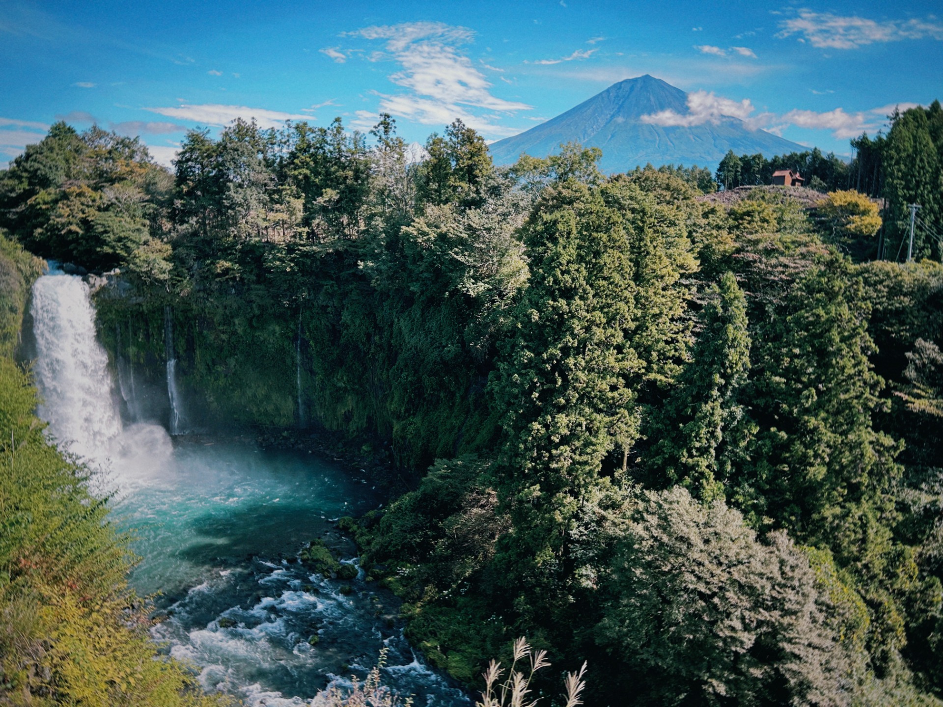 Cascada rodeada de bosques con el Monte Fuji al fondo