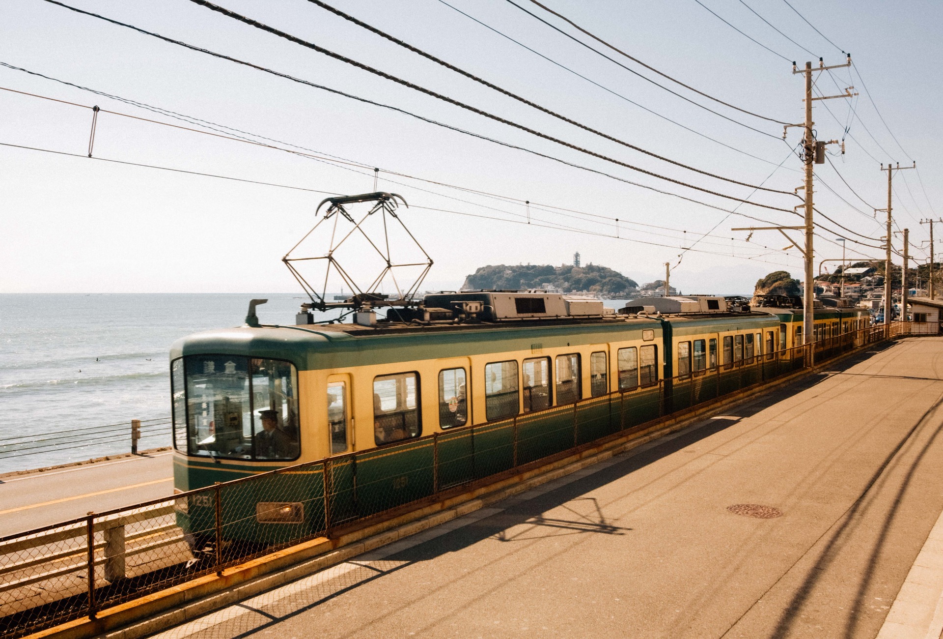 El tranvía Enoden circulando junto al mar en la costa de Kamakura, con la isla de Enoshima al fondo.