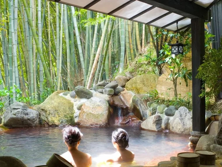 Pareja bañándose en un onsen privado al aire libre entre rocas y un bosque de bambú