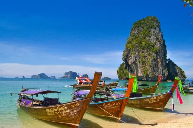 Barcas de cola larga en una playa de Tailandia con un islote de roca al fondo